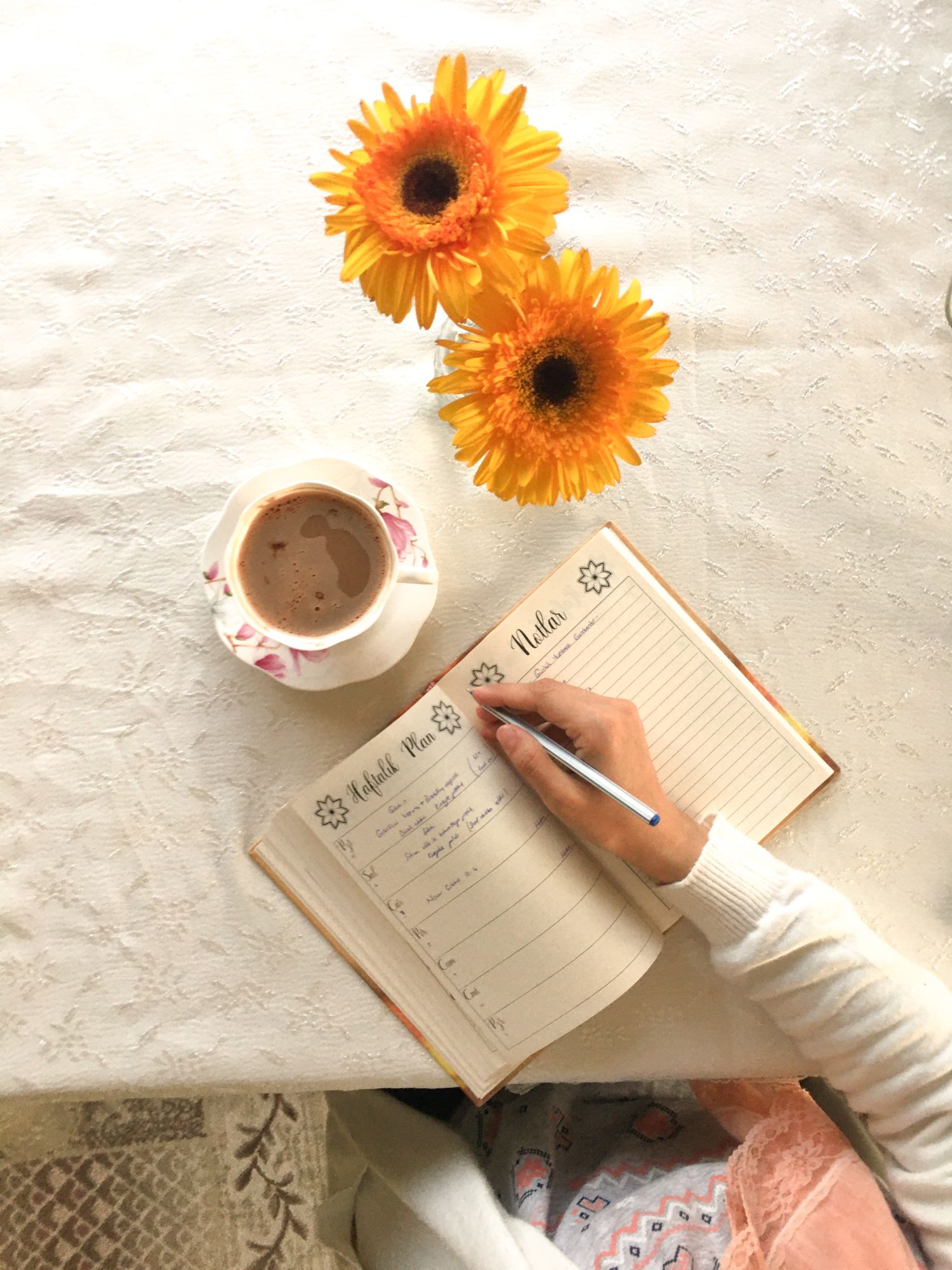A person writing in a planner beside coffee and flowers