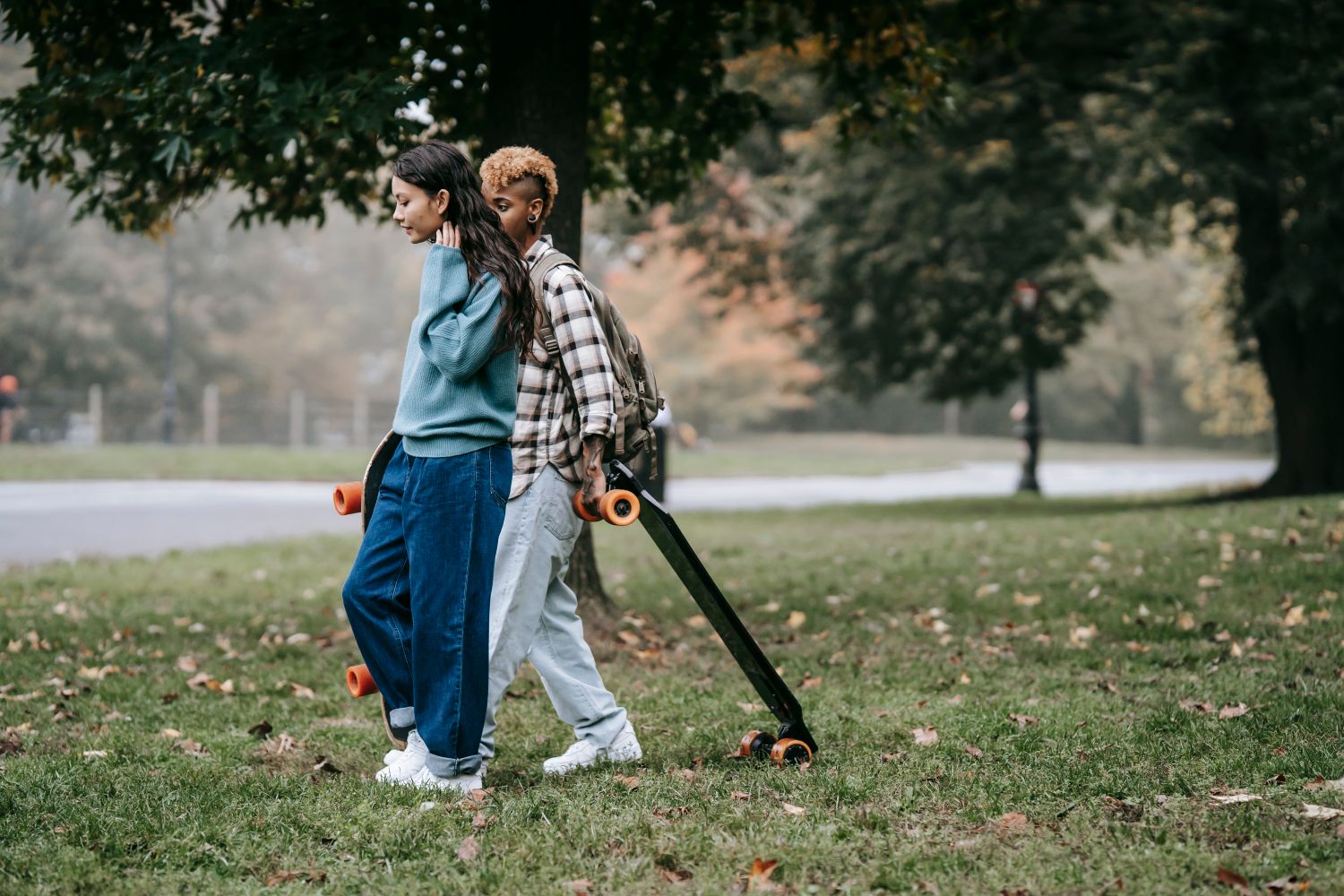 Two friends walking through a park with skateboards